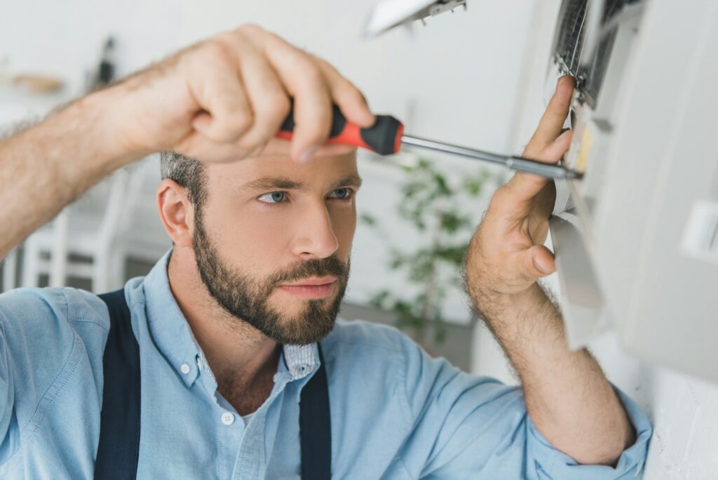 repairman fixing air conditioner with screwdriver at home